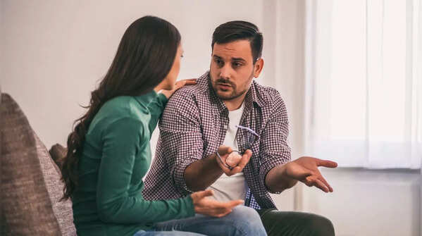 A couple having conversation, one looking serious and the other avoiding eye contact.